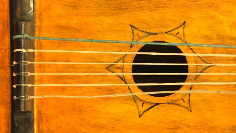 Worn guitar body with tattered strings and star design around the sound hole