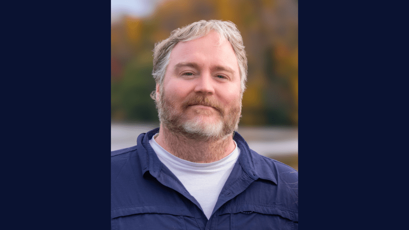 person wearing a white shirt and blue button up shirt standing outdoors for photo