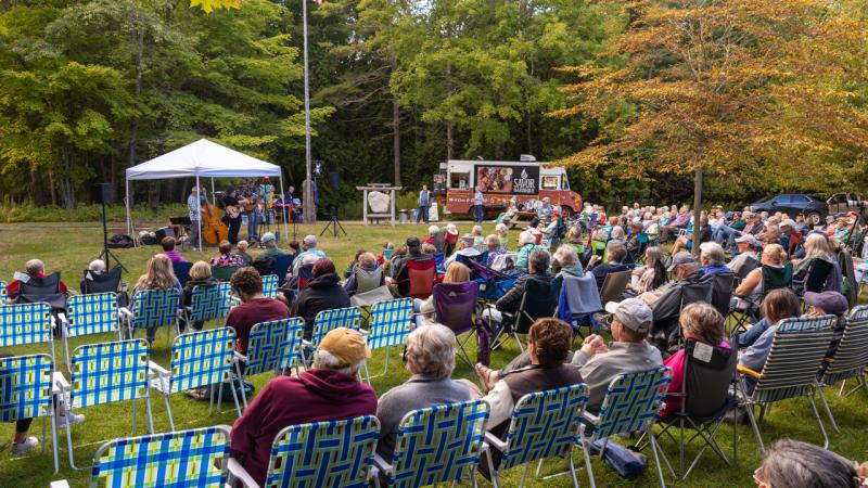 a crowd seated on the lawn in front of the chapel taking in a concert