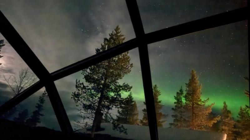 Green northern lights glow in the night sky above a glass igloo in northern Finland.