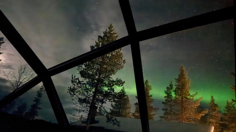 Green northern lights glow in the night sky above a glass igloo in northern Finland.