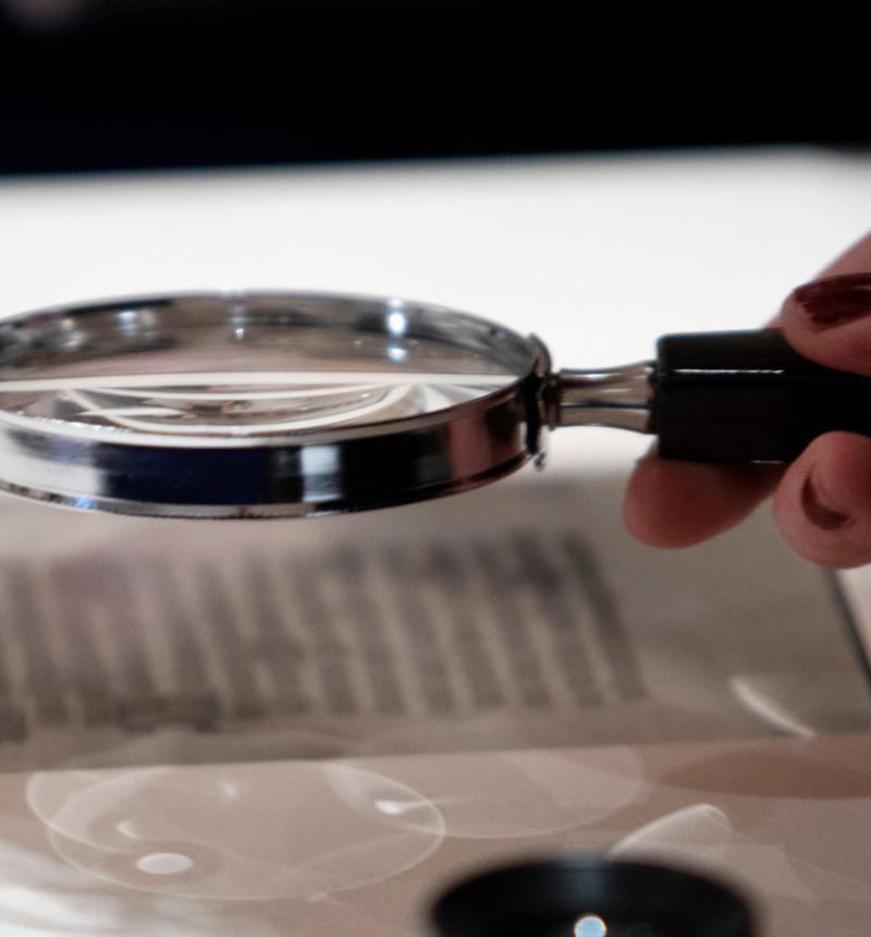 Hand holding a magnifying glass inspects parchment