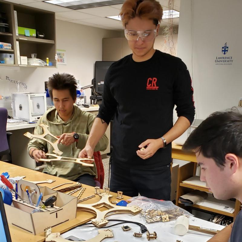 Group of three students assembling laser-cut wooden pieces in the makerspace.