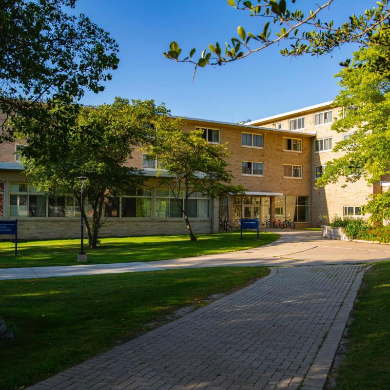 two brick roads leading to three-story brick building with green trees in foreground