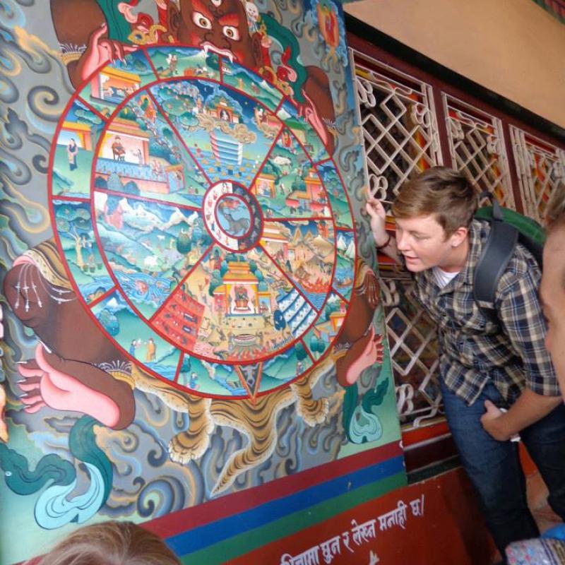 Connie in Nepal with students, contemplating a painting of the Buddhist cycle of life and rebirth