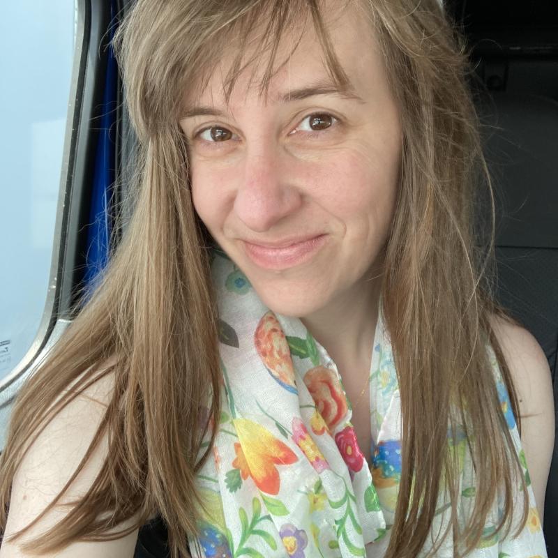 The image is of benignly smiling face. She is wearing a colorful scarf. A truck window is visible over the right shoulder.