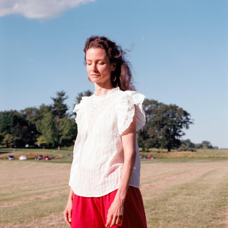 Marion Ramirez standing in an empty field wearing a white loose shirt and loose red pant.