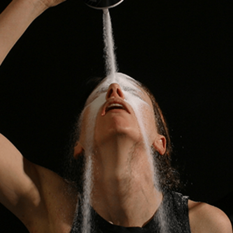 Dancer and performer Michelle Ellsworth pours a bowl over her face with eyes closed, salt spilling to either side of her open mouth.