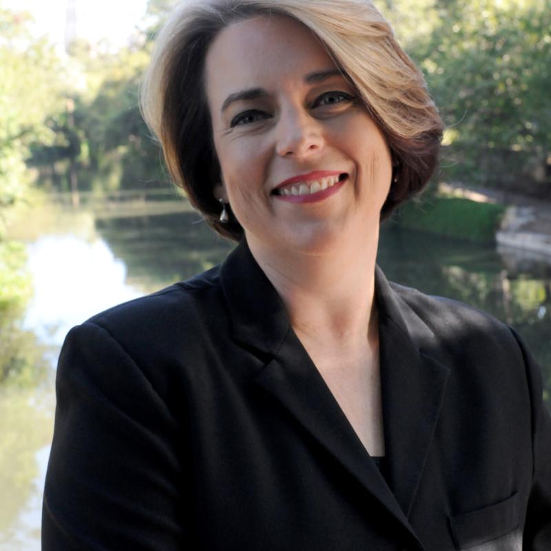 Photo of Professor Kristin Roach wearing a black jacket in sunshine by a river. Photo credit Kristian Jaime.