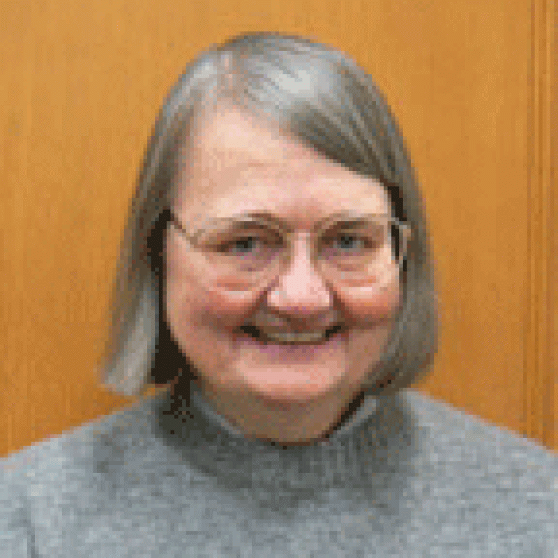 Woman with short gray hair smiling, wearing gray sweater.
