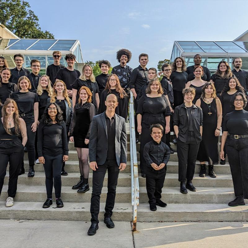 Steve Sieck poses on Conservatory steps with Concert Choir members, all are dressed in concert black and smiling