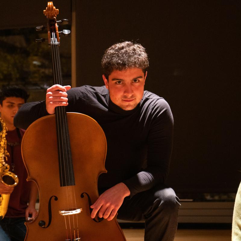 Cellist on one knee holds his cello during an improvised performance