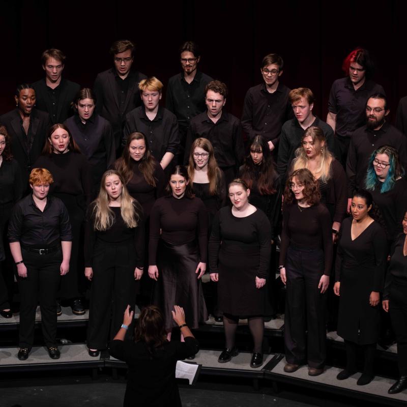 Vocalists in concert black sing on risers with their faces lit against the darkness of the auditorium