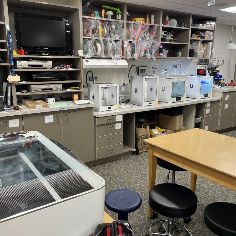 Inside the makerspace with a view of 4 3D printers, the laser cutter, a table, and digitizing equipment.