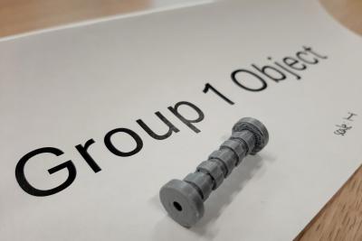 3D printed object: a small gray rod with ridges