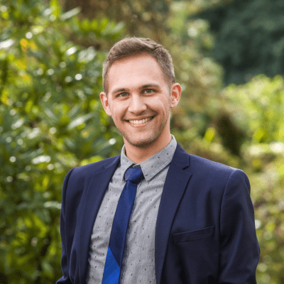 Joe Johnson '17, smiling, in a dressy grey shirt with a dark blue tie and jacket