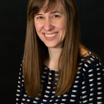 Smiling pale woman with brown hair, teacups on dress.