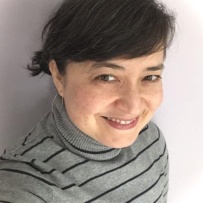 head shot of smiling, mixed race, black haired woman in grey turtleneck with black stripes