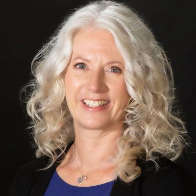 Headshot of Lori Fares, white woman with white hair in a blue blouse and black blazer.