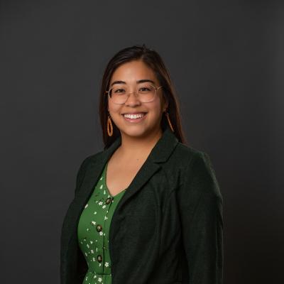 Sarah, an Asian American woman, wearing a green dress and dark green blazer