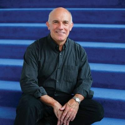 Smiling white man sitting on blue carpeted stairs.