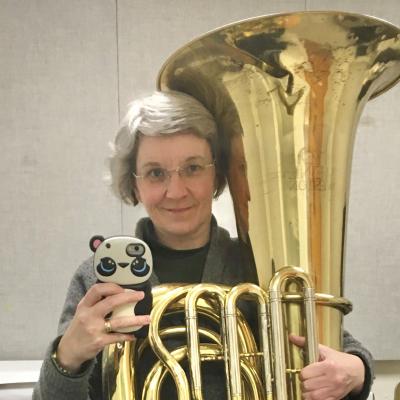 Heather, a middle-aged woman with glasses and gray hair, holding a tuba and taking a mirror selfie