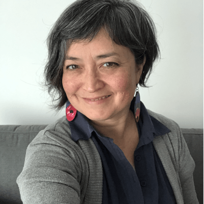 head shot of smiling, mixed race Asian woman in blue shirt collar with grey sweater and red flower earrings