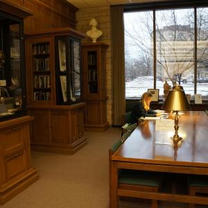 Student sitting at a long wooden table with gold lamps, surrounded by wooden and glass cabinets full of books and Lincoln ephemera.