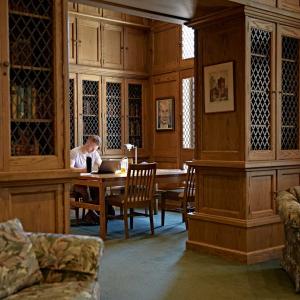 Person sitting at a table in the Milwaukee Downer room, which contains wood paneling and wood cabinetry with decorative metal doors, which holds the rare book collection.
