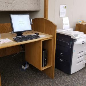 Computer at a table with print release software next to a large printer.