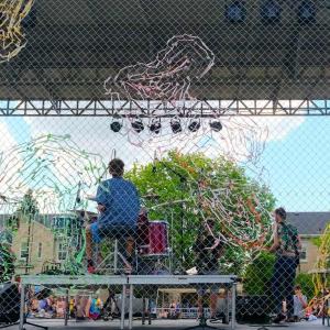 Three band members play on outdoor stage.