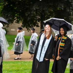 Two graduates stand under an umbrella and smiling during the parade.