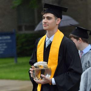 Graduate walking with a goldfish swimming in a small fishbowl.