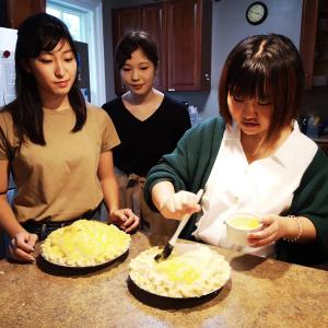 Three students in kitchen brushing pie crust with egg wash.