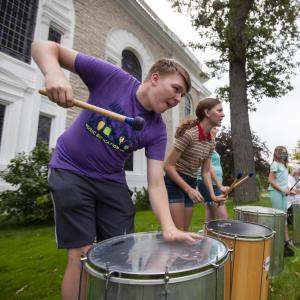 Boy plays large drum outside.