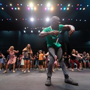 A man leading a group of families in a dance workshop.
