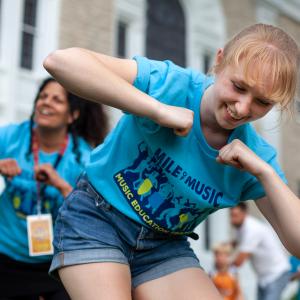 Two women in blue T-shirts leading a group of families in dance.