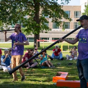 Two men in purple T-shirts leading a group of families in a didjeridu workshop.