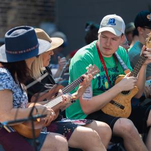 A man teaching two women how to play the ukulele.