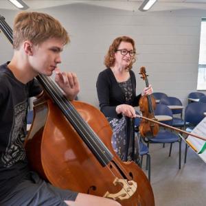 LSMI Samantha George points to music with violin bow at practices with cello student. 
