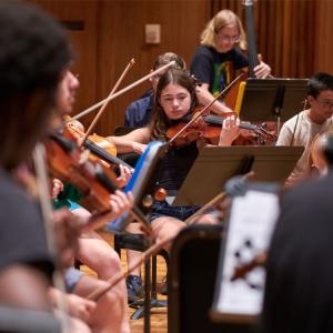 Several LSMI students practice on stringed instruments in Harper Hall.