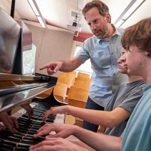 LSMI faculty Michael Mizrahi points to music while two students practice piano