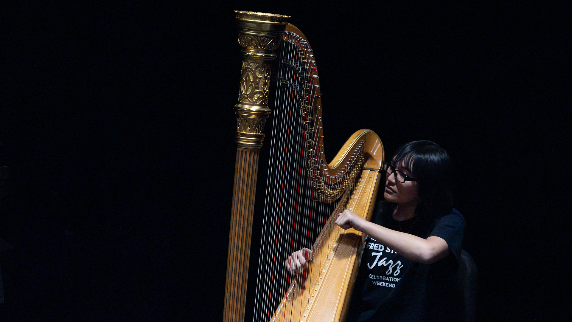 A person playing a golden harp on a dark stage.