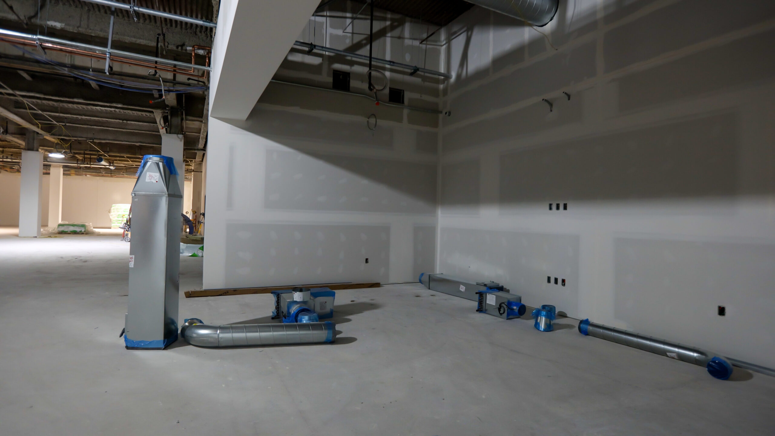 Unfinished interior with exposed drywall and ductwork parts on the floor, showing ongoing construction or renovation in a commercial space.