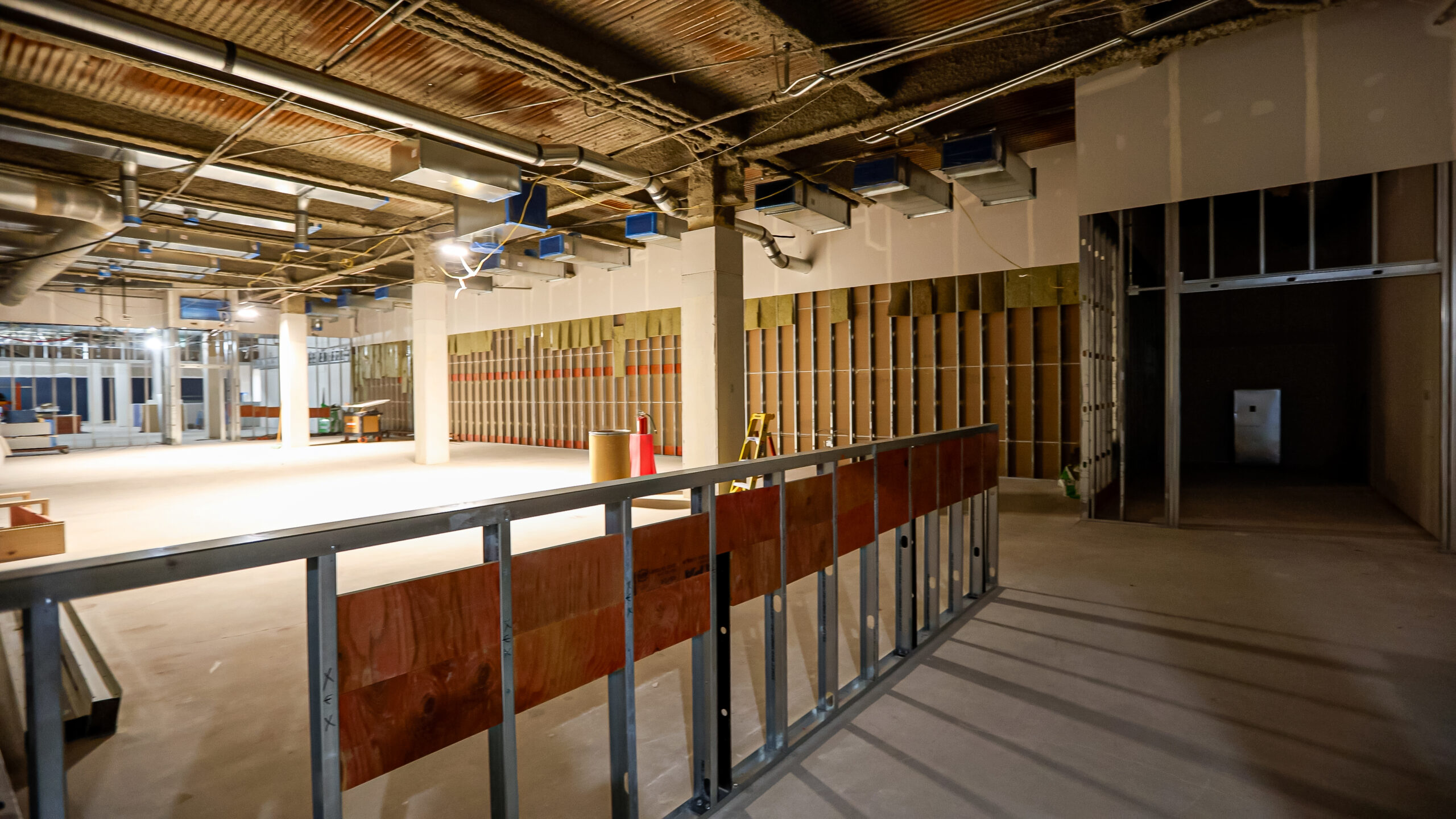 Interior of a commercial building under construction, with exposed ceiling, unfinished walls, and construction materials scattered around the open space.