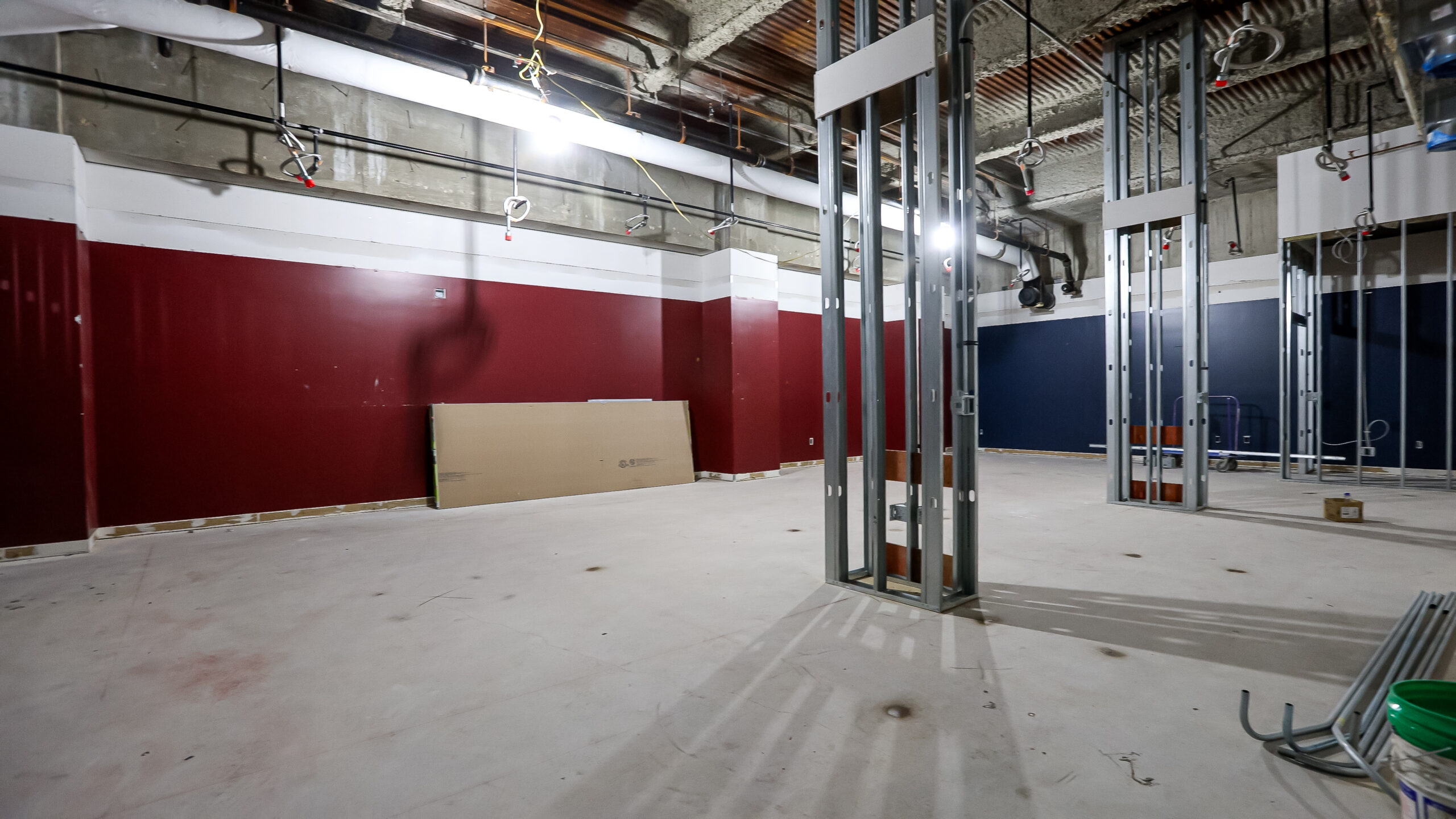 Unfinished room with red walls, exposed ceiling pipes, metal framing, and scattered construction materials on the floor.